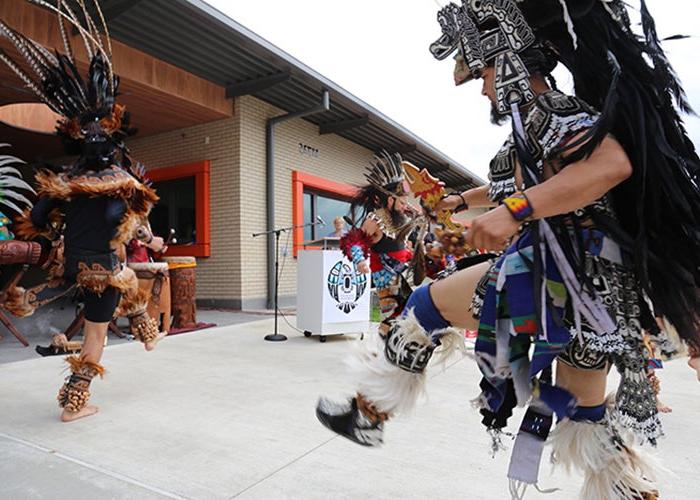 people in native dress dance in front of a 1 story building