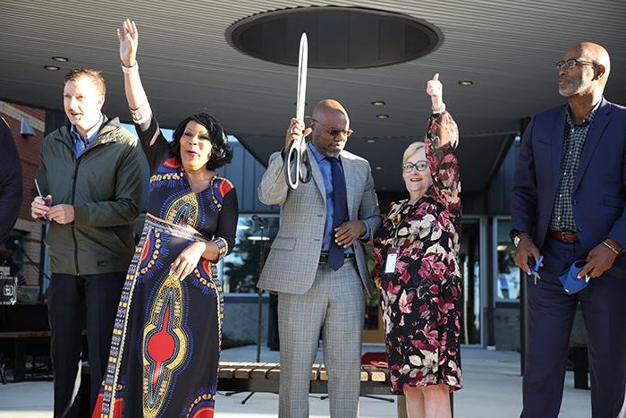 five people hold pieces of red ribbon and scissors with their hands up to cheer