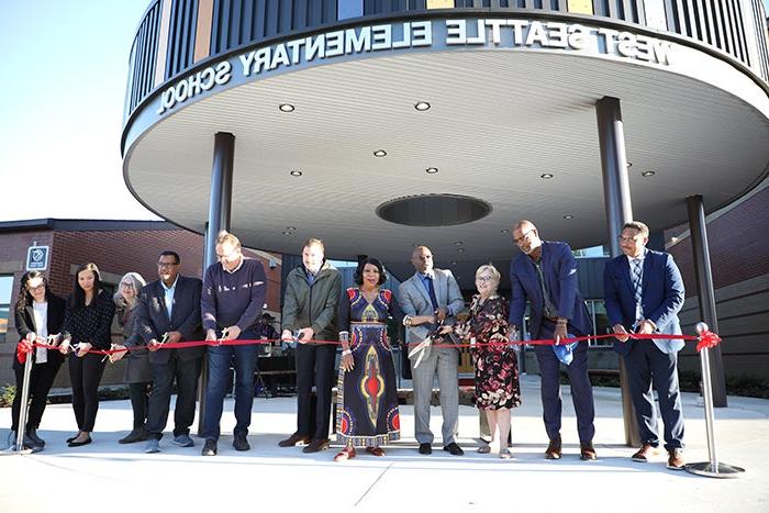 a group of people line up behind a red ribbon. all hold scissors. a circular canopy is above and behind them